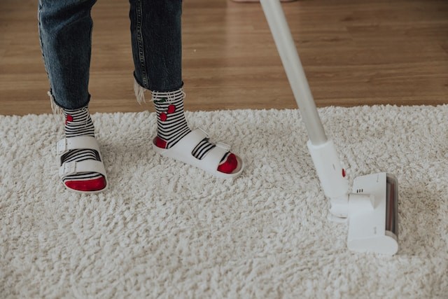 person cleaning the carpet by vacuun cleaner