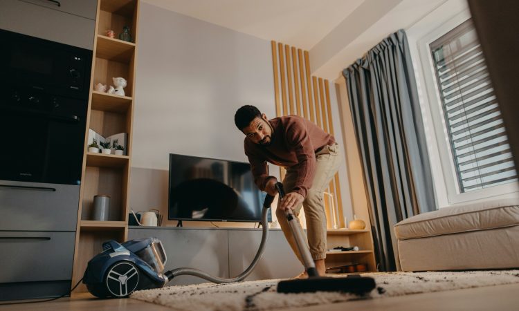 a-young-man-hoovering-carpet-with-vacuum-cleaner-in-living-room